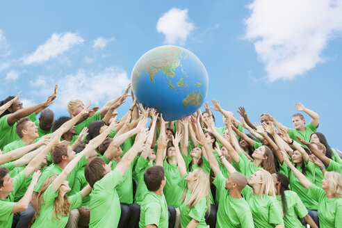 Team in green t-shirts lifting globe overhead - CAIF01180