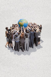 Crowd of business people in huddle lifting globe overhead - CAIF01221