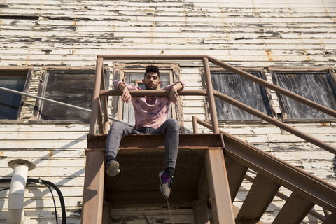 Porträt eines stilvollen jungen Mannes, der auf einer Treppe im Freien sitzt, lizenzfreies Stockfoto