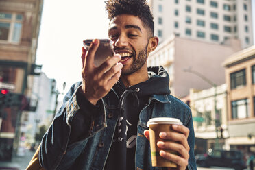 Porträt eines stilvollen jungen Mannes mit Kaffee und Smartphone auf der Straße - SUF00474