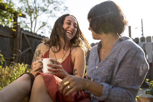 Two happy young women talking in backyard - SUF00480