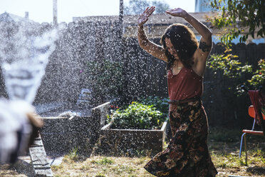Water splashing on young woman in backyard - SUF00485