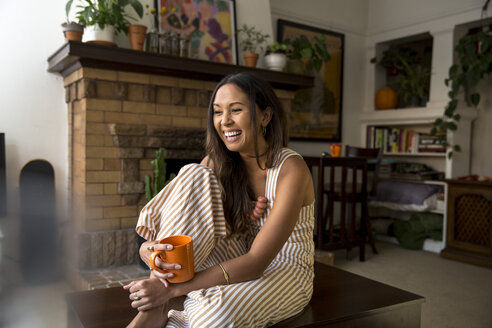 Laughing young woman with coffee mug sitting at home - SUF00490