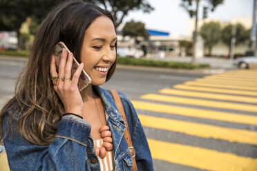 Lächelnde junge Frau, die auf der Straße mit ihrem Smartphone spricht - SUF00498