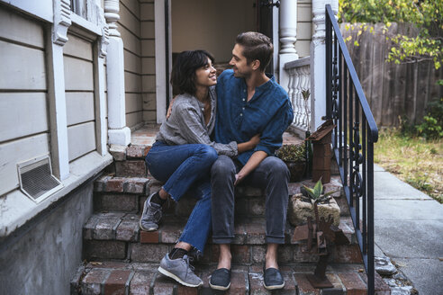 Happy couple sitting on stoop embracing - SUF00512