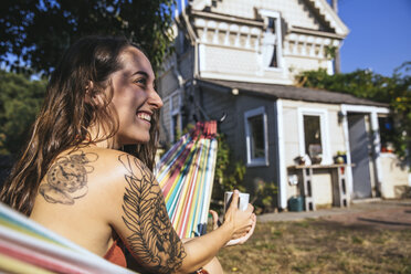 Glückliche junge Frau mit Tattoo in der Hängematte - SUF00522