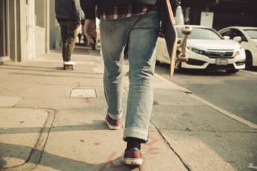 Low section of man walking on sidewalk with skateboard - SUF00527