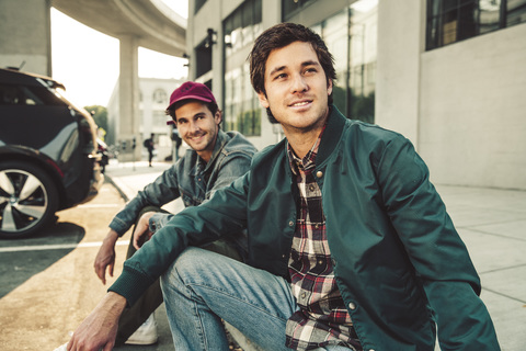Zwei lächelnde junge Männer sitzen auf dem Bürgersteig, lizenzfreies Stockfoto