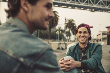 Zwei lächelnde junge Männer sitzen im Freien und unterhalten sich - SUF00534