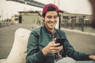 Porträt eines lächelnden jungen Mannes, der ein Mobiltelefon benutzt - SUF00535