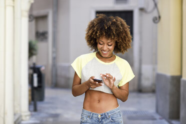 Smiling woman with afro hairstyle using smartphone outdoors - JSMF00005