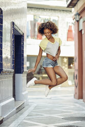 Happy woman with afro hairstyle jumping in a lane - JSMF00008