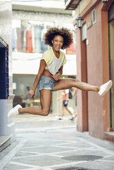 Glückliche Frau mit Afrofrisur, die in einer Gasse springt - JSMF00009