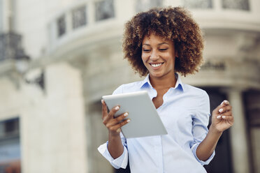 Smiling woman with afro hairstyle using tablet in the city - JSMF00010