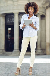 Porträt einer Frau mit Afrofrisur, die ein Tablet in der Stadt hält - JSMF00011