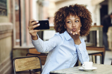 Woman with afro hairstyle sitting in outdoor cafe taking a selfie - JSMF00016