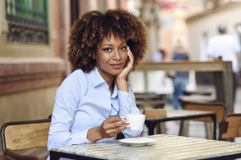 Porträt einer lächelnden Frau mit Afrofrisur in einem Café im Freien, lizenzfreies Stockfoto