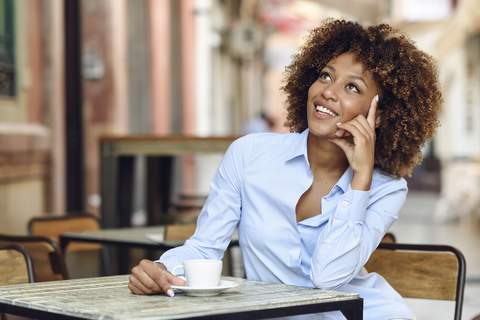 Lächelnde Frau mit Afrofrisur sitzt in einem Café im Freien, lizenzfreies Stockfoto