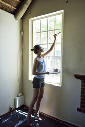 Junge Frau renoviert ihr Haus und streicht den Fensterrahmen - ECPF00186
