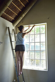 Junge Frau renoviert ihr Haus und arbeitet am Fensterrahmen - ECPF00187