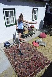 Glückliche junge Frau beim Staubsaugen des Teppichs im Freien - ECPF00195