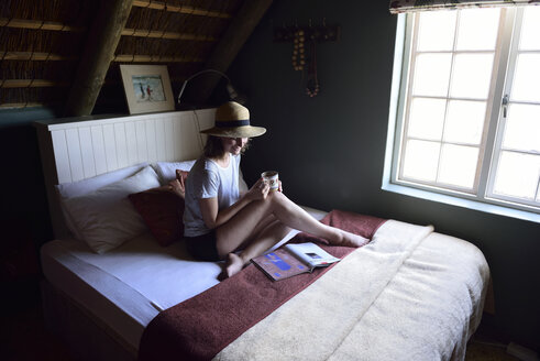 Lächelnde junge Frau auf dem Bett sitzend mit Kaffeetasse und Zeitschrift - ECPF00197