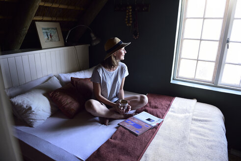 Lächelnde junge Frau auf dem Bett sitzend mit Kaffeetasse und Zeitschrift - ECPF00198