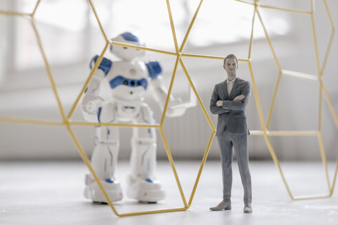 Miniature businessman figurine standing in front of robot with laptop seperated by structure - FLAF00146