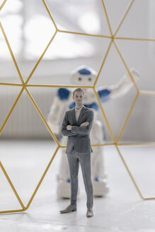 Miniature businessman figurine standing in front of robot seperated by structure - FLAF00148