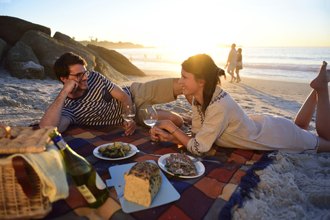 Happy couple having a picnic on the beach at sunset stock photo