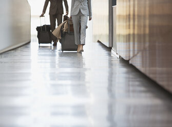 Geschäftsmann und Geschäftsfrau ziehen Koffer die Rampe im Flughafen hinunter - CAIF01248