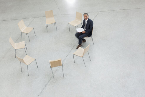 Porträt eines lächelnden Geschäftsmannes, der in einem Kreis von Stühlen sitzt - CAIF01255
