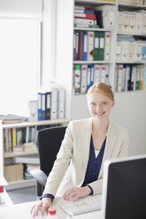 Porträt einer lächelnden Geschäftsfrau am Schreibtisch im Büro - CAIF01270