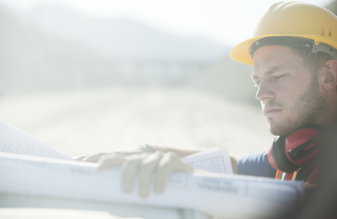 Arbeiter beim Lesen von Bauplänen auf der Baustelle, lizenzfreies Stockfoto