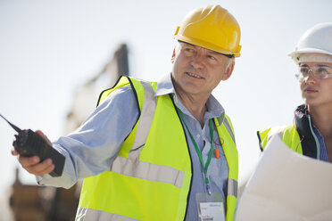 Geschäftsleute mit Schutzhelmen im Gespräch auf der Baustelle - CAIF01343