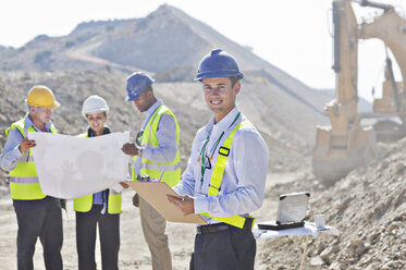 Businessmen reading blueprints in quarry - CAIF01364