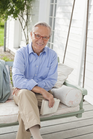 Lächelnder Mann auf Veranda-Schaukel sitzend, lizenzfreies Stockfoto