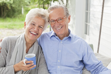 Smiling couple sitting on porch swing - CAIF01445