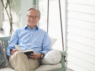 Mann liest Buch auf Veranda-Schaukel - CAIF01446