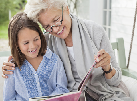 Frau und Enkelin lesen auf einer Veranda-Schaukel, lizenzfreies Stockfoto