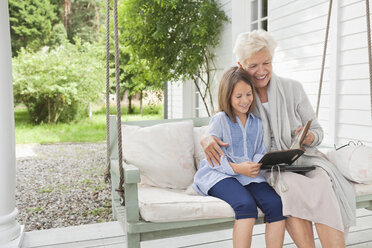 Frau und Enkelin lesen auf einer Veranda-Schaukel - CAIF01461