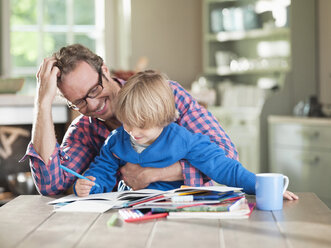 Father and son doing homework at kitchen table - CAIF01475