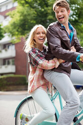 Couple riding bicycle together on city street - CAIF01531