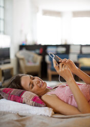 Woman listening to mp3 player on bed - CAIF01532