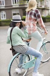 Women riding bicycle together on city street - CAIF01534