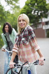 Women standing on bicycles on city street - CAIF01547