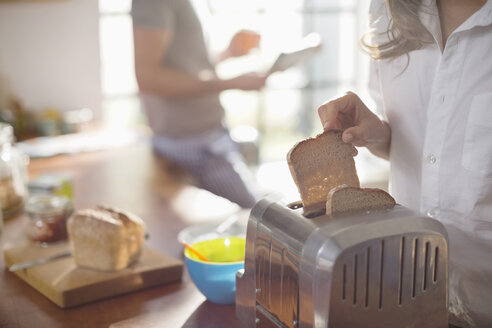 Frau steckt Brot in den Toaster - CAIF01549