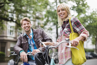 Couple standing on bicycles on city street - CAIF01554