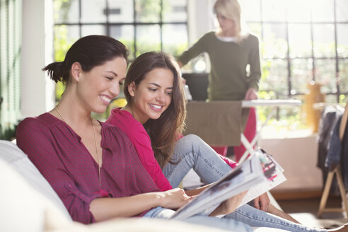 Frauen lesen gemeinsam eine Zeitschrift auf dem Sofa - CAIF01563