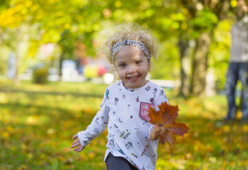 Happy little girl running with autumnal leaf in park - WWF04196